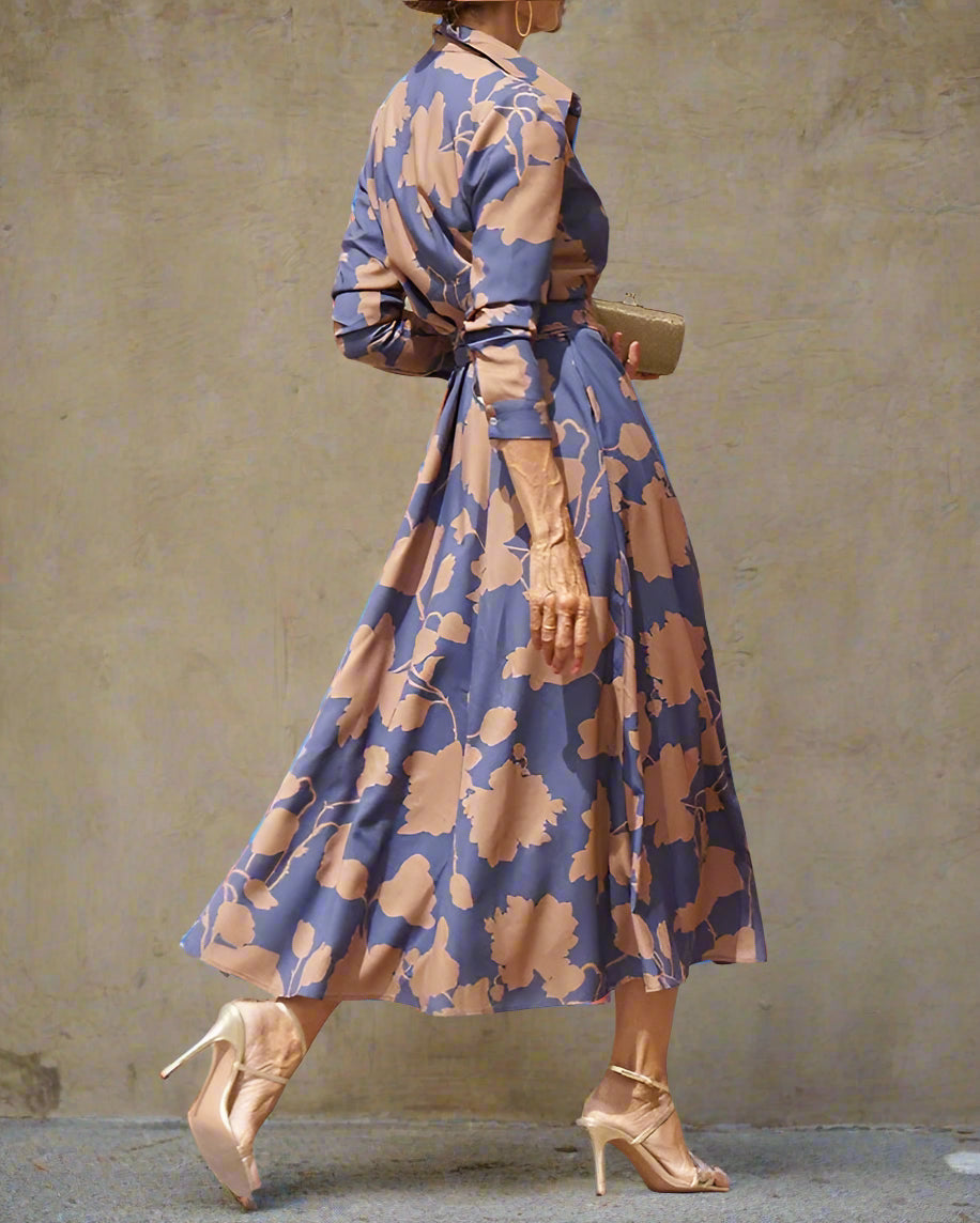 Woman in a blue floral dress standing in front of a stone building.