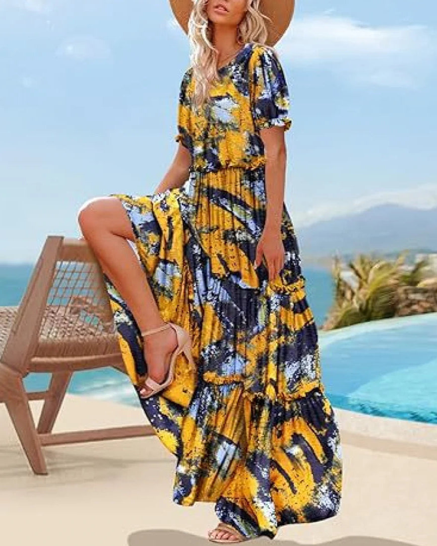 Woman in a yellow and blue patterned dress sitting by a pool with a scenic background.