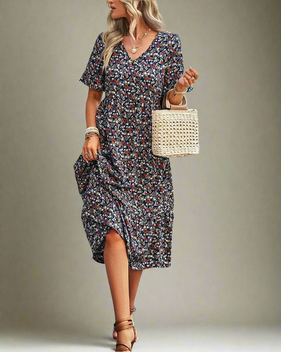 Woman in a floral dress walking outdoors holding a woven bag.